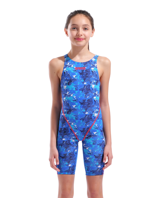 A young girl stands against a white background, smiling slightly in the Arena Girls Powerskin ST Next - limited edition - splashy by Arena, an eco-friendly racing suit made from recycled fabrics that exudes confidence and promotes sustainability.